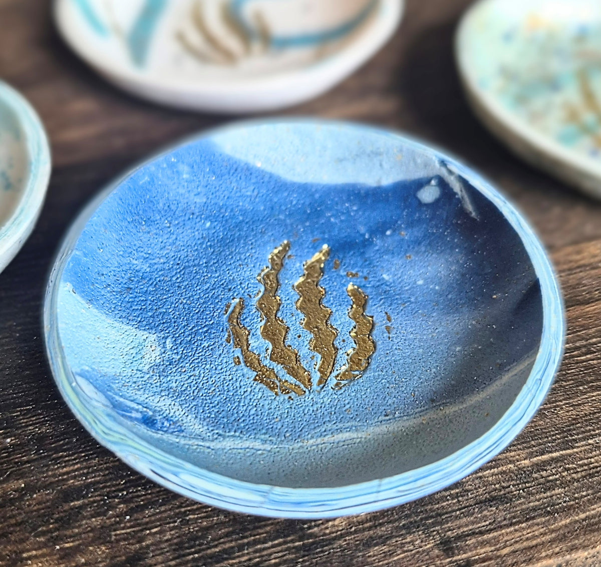 Sefara Jewellery handcrafted coastal trinket dishes featuring Scottish seascape colours and textures with gold leaf seaweed detailing, approximately 6cm in diameter.