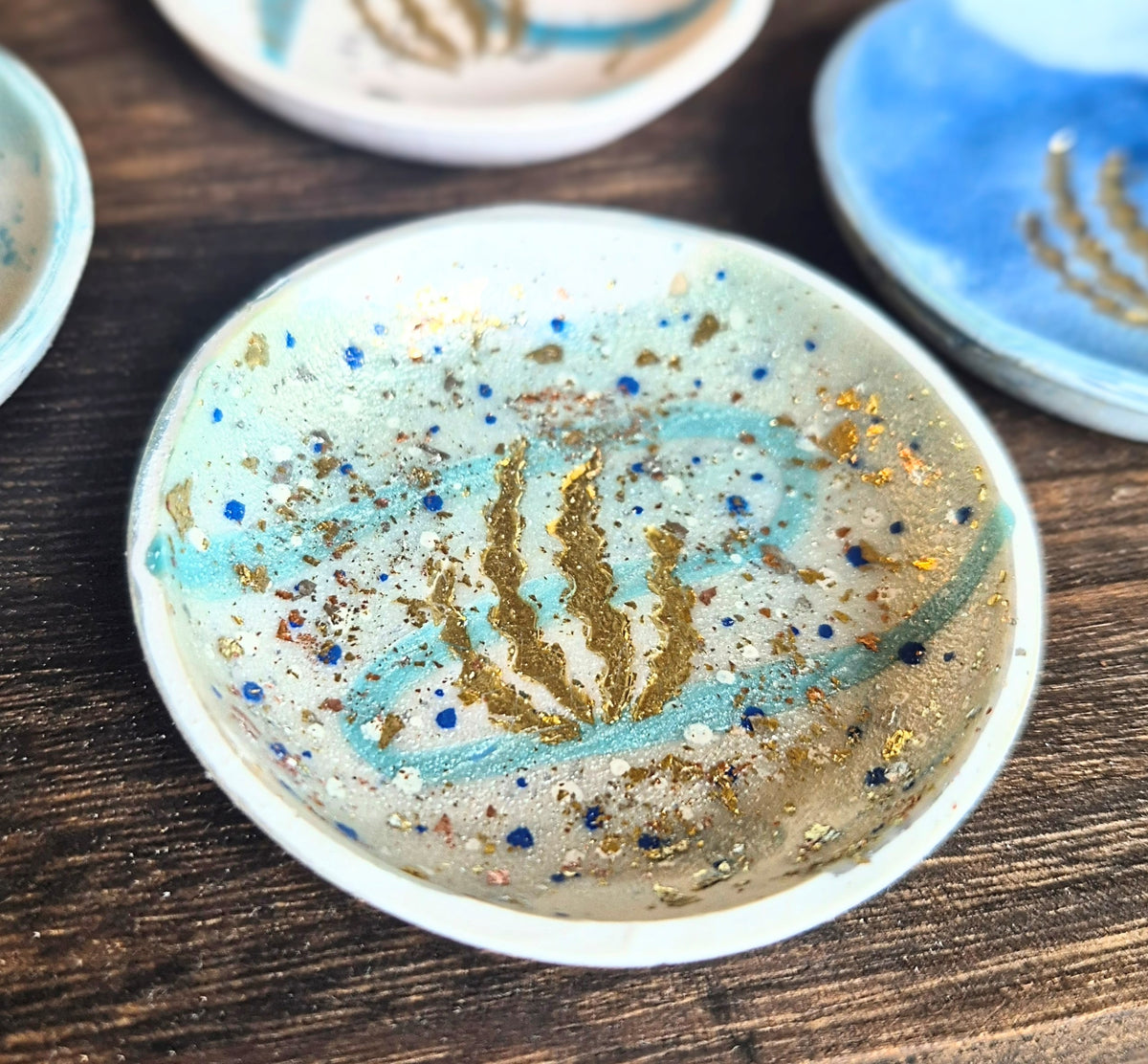 Sefara Jewellery handcrafted coastal trinket dishes featuring Scottish seascape colours and textures with gold leaf seaweed detailing, approximately 6cm in diameter.
