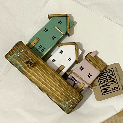 Handcrafted trio of wooden houses on block with rustic metal details in green, pink, and white