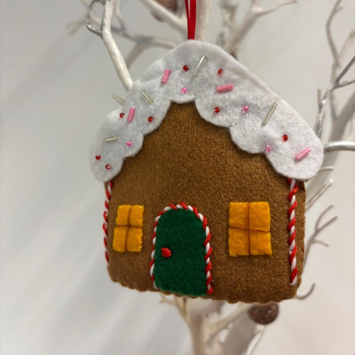 Felt gingerbread house ornament with white roof on a branch