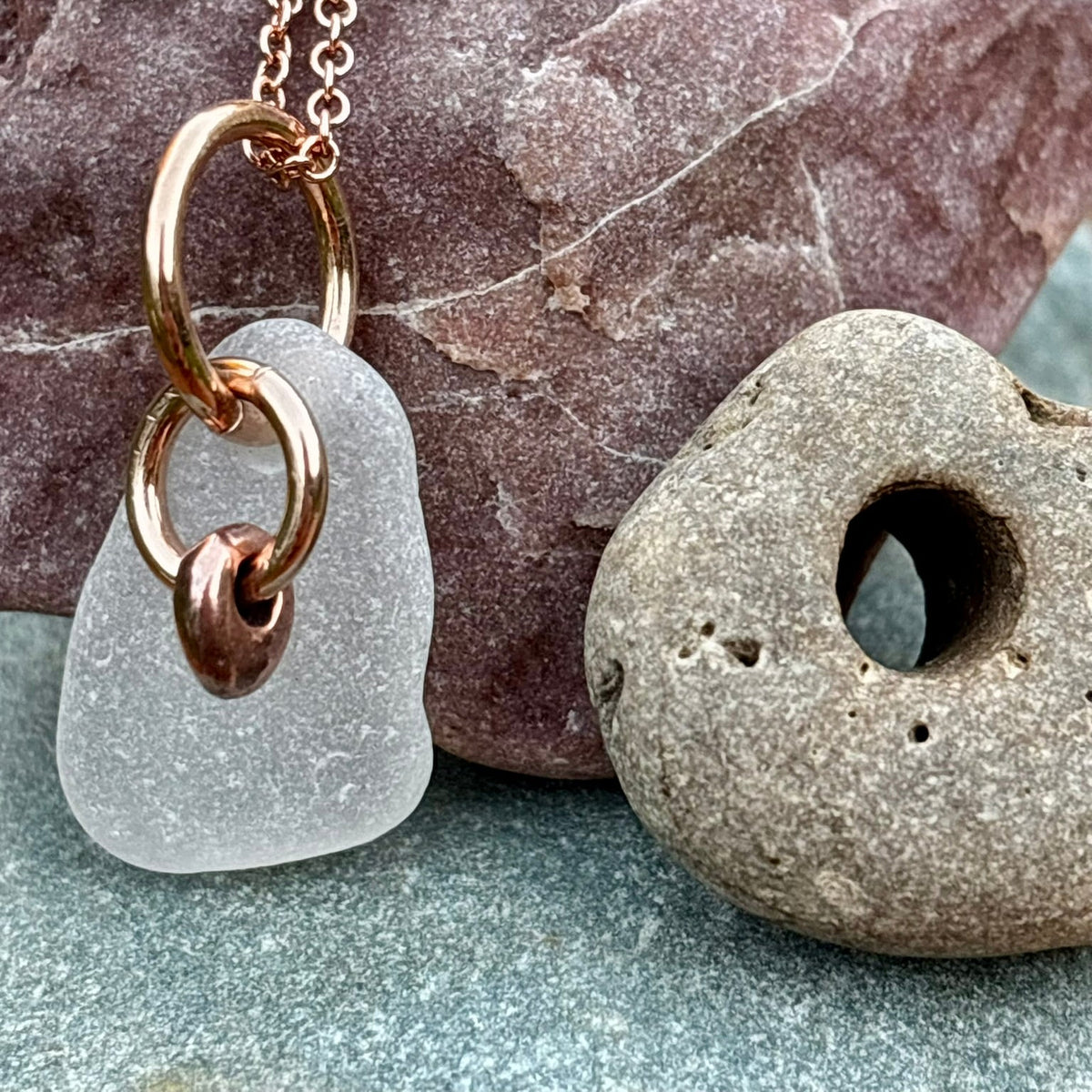Rowan Berry Jewellery sea glass and hag stone necklace featuring frosted seafoam sea glass, a handcrafted copper hag stone and two bronze hoops on a rose gold-plated chain.