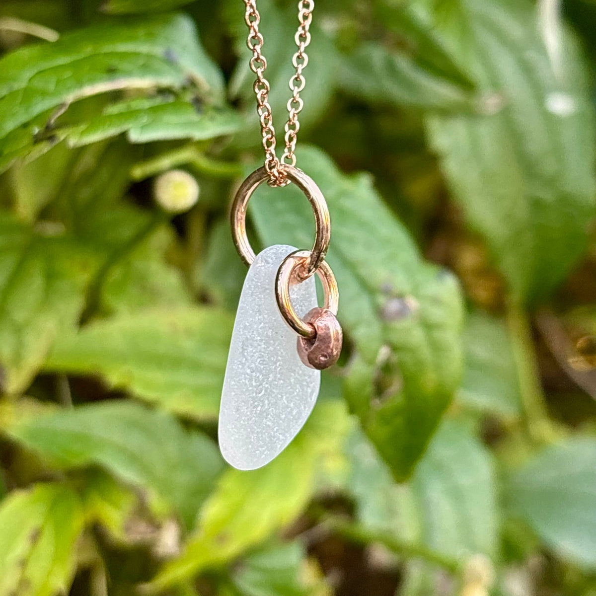 Rowan Berry Jewellery sea glass and hag stone necklace featuring frosted seafoam sea glass, a handcrafted copper hag stone and two bronze hoops on a rose gold-plated chain.