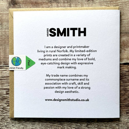 Back of white card with text about the designer and printmaker named Design Smith on a wooden surface