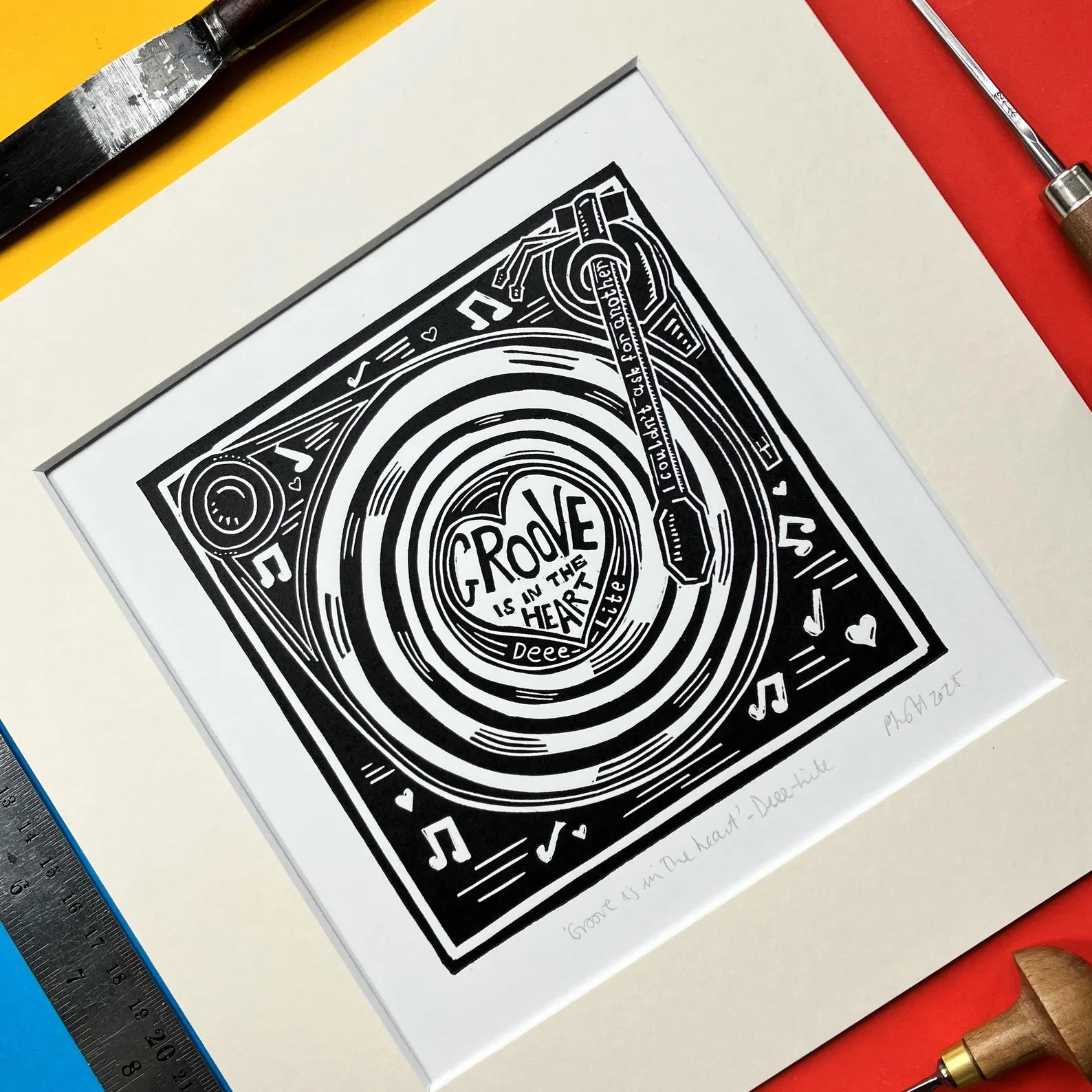 Framed black and white Pamela Scott Groove Is In The Heart lino print artwork with tools on a colourful background